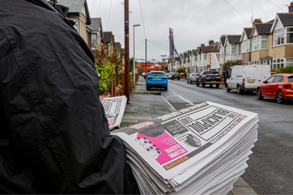 The image shows a person holding a stack of The Blackpool Lead on a street in Blackpool.
